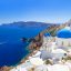 A view of white buildings with blue domed roofs on an oceanside cliffside.