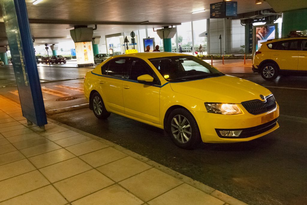 A yellow Athens Airport taxi parked outside airport arrivals.