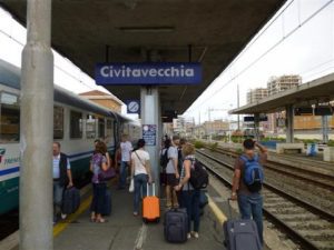 A regional train arriving at a platform at Civitavecchia Train Station, with people standing on the platform and a blue 