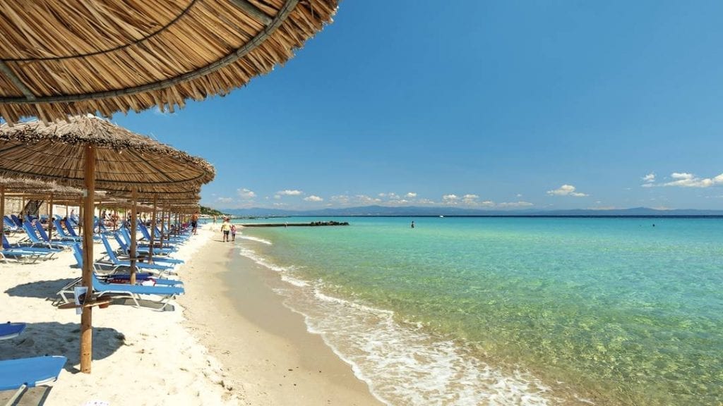 halkidiki beach. Crystal clear water with palapa shade and blue sun loungers.