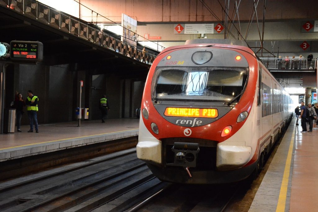 A red Renfe commuter train arriving at platform of the airport.