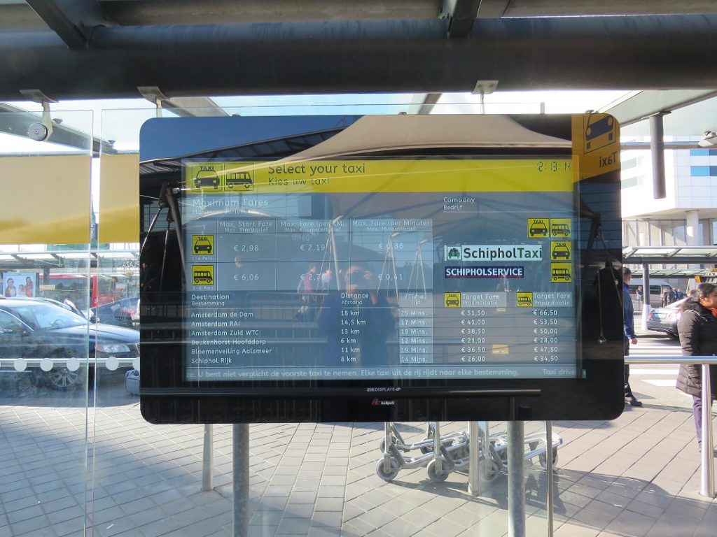 Amsterdam taxi information, an electronic screen display hanging in front of a window in arrivals.