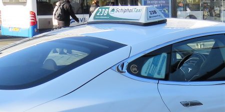 The roof of a white Amsterdam taxi with a 'Schiphol taxi' sign on the top.