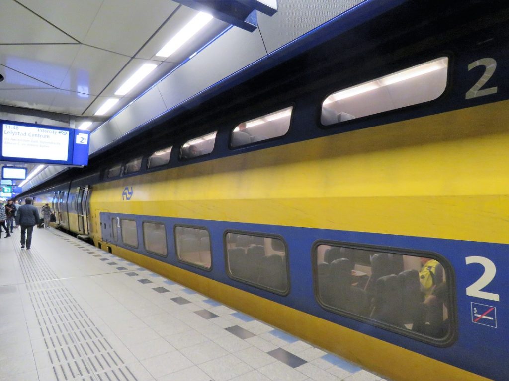 A yellow and blue Amsterdam Airport train waiting on the platform