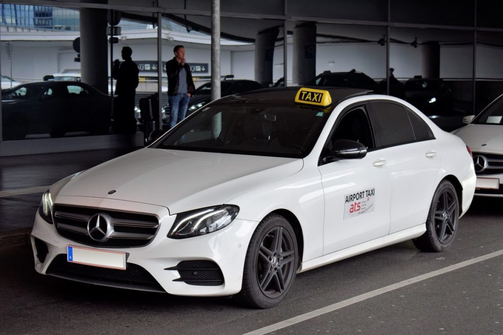 A white Vienna Airport taxi (Sedan) parked in a parking space outside the airport.