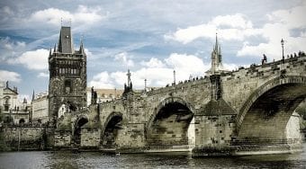 View of Charles Bridge and its tower from below, with cloudy skies above in Prague.