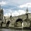 View of Charles Bridge and its tower from below, with cloudy skies above in Prague.