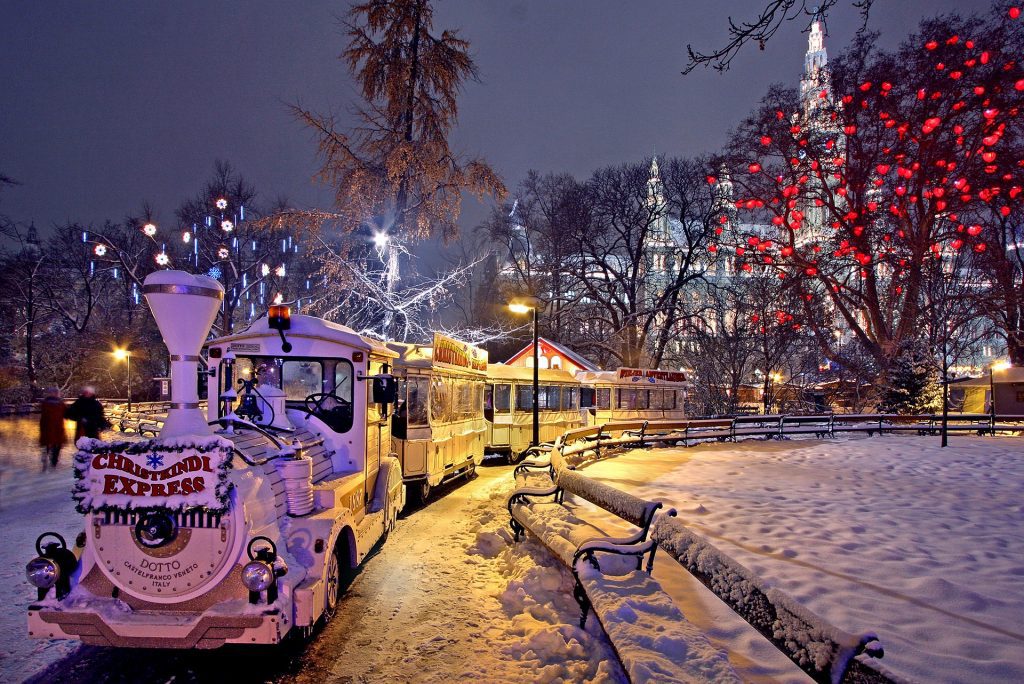 A small train ride stationed in the snow at a Vienna Christmas market with lots of lights.