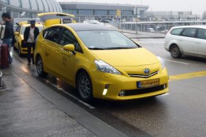 Budapest Airport taxi - Welcome Pickups A yellow Budapest Airport taxi parked outside the airport, with the car boot open.