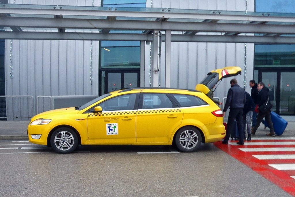 A yellow Budapest Airport taxi with the boot open as the driver waits for the passenger to place the luggage inside.