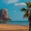 Scenic view in Alicante, Spain with rock face and palm tree on a sandy beach.