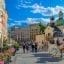 A horse drawn carriage stops alongside pedestrians walking next to rows of flowers and buildings in Krakow.