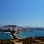 A clear daytime view of Naxos town and its coastline, with the Aegean Sea in the foreground and the island’s whitewashed buildings rising in the distance. Just a short drive from this scenic harbor lies Naxos Airport, the island’s main air gateway for domestic travelers.