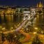 Budapest city lit up at night with a bridge crossing over a river and a large church in the background.