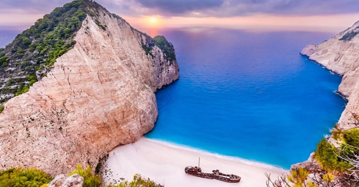 Scenic view of Navagio Beach at sunset, with dramatic white cliffs, turquoise waters, and the famous shipwreck on the sand—an iconic stop often included in a transfer from Zakynthos Airport to the island’s top attractions.
