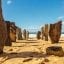 A beach in Vilamoura with large stones standing upright in the sand and blue water and skies behind.