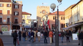 A photo of Mestre Train Station, with people on the streets and a clock tower in the background.