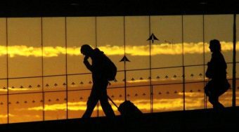 A silhouette of a person walking through Rome Airport with their luggage and the setting sun in the background.