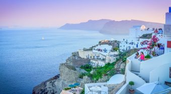 View from Oia, with buildings on the cliff edge looking out towards a blue sea at sunset.