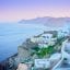 View from Oia, with buildings on the cliff edge looking out towards a blue sea at sunset.