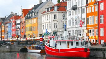Colourful houses along a canal in Copenhagen with a red and white boat floating past.