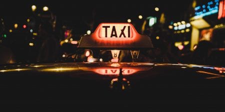 A glowing taxi roof sign on top of a taxi at night.