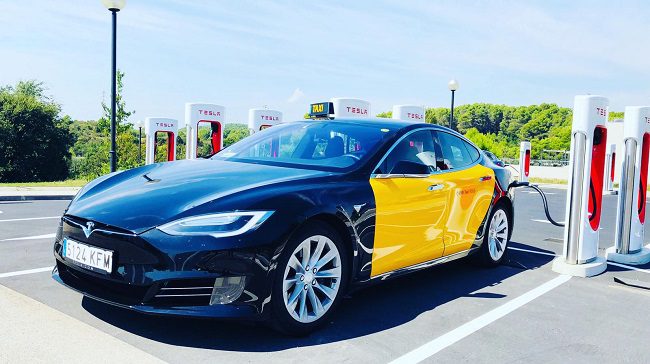 barcelona-taxi-tesla Side/front view of a black and yellow Barcelona taxi tesla parked at a charging station.