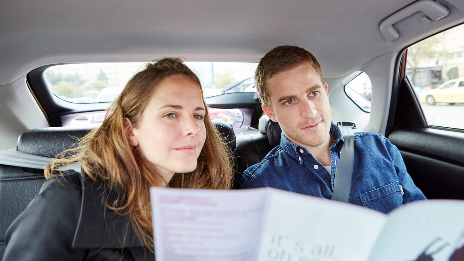 man and woman in the back seats of a taxi checking a map