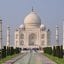 Photo of Taj Mahal, with view of paved walkway and green grass and hedges against a blue sky