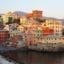 View of colourful homes and buildings situated close to the water in Genoa, Italy with mountains behind.
