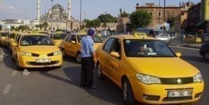 Row of yellow Istanbul taxi cars lined up on a city street during daylight, with a mosque visible in the background, highlighting a common mode of transport for navigating Istanbul.