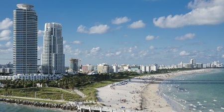 Coastline of Miami beach, sky towers, and bridge under a cloudy blue sky.