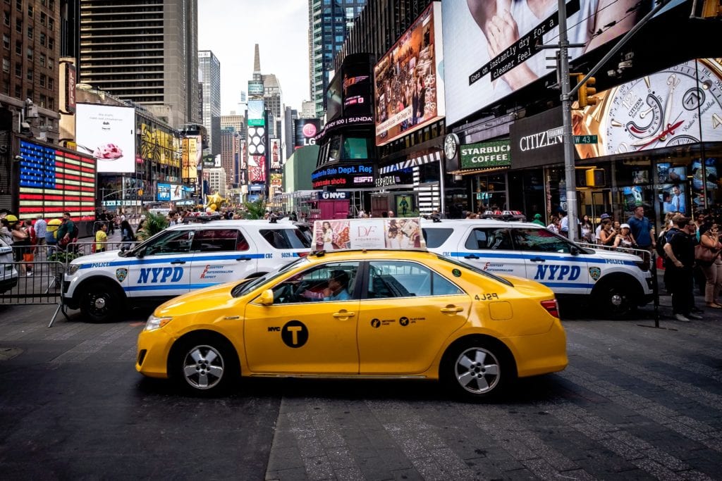 Yellow LaGuardia Airport Taxi in the streets of New York with two police vehicles parked behind it.