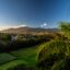 A view of San Jose with rolling green fields infront and mountains behind, with blue skies above.