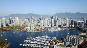 An aerial view of Vancouver City looking over the bay with high-rise buildings in the background and the harbour in the foreground.