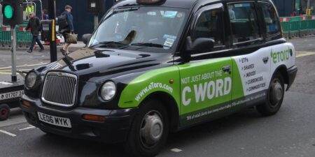 A front/side view of a black Hackney Manchester cab, with green advertising across the side, stopped at a traffic light.