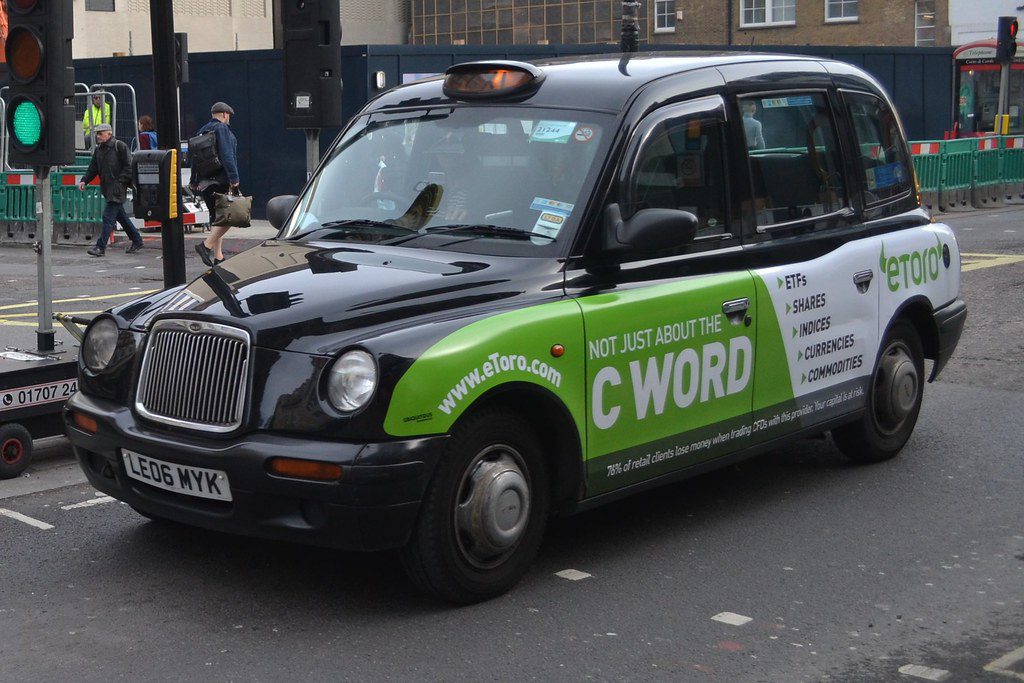 Manchester taxi black cab A front/side view of a black Hackney Manchester cab, with green advertising across the side, stopped at a traffic light.