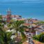 traditional white mexican buildings with terracota tile roofs, palm trees on the foreground and blue sea in the background