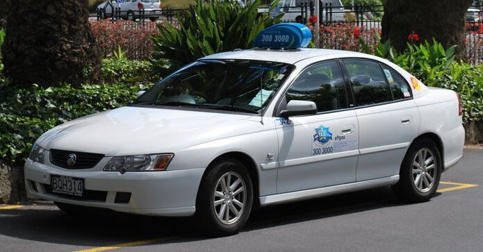 white car with blue taxi sign with number on the roof and taxi emblem on the door