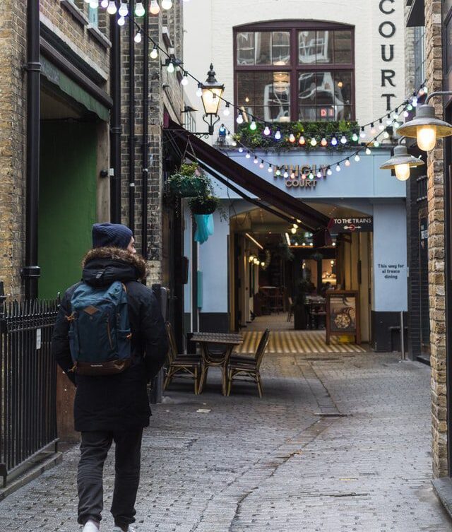 man dressed with winter clothes walking in narrow paved street in central london