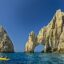 View of rocky formations coming up out of the sea, with blue skies above and a small yellow boat in the water.