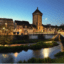 A castle and old buildings lit up at night along a river.