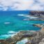 Aerial view of cliffs edge next two clear blue body of water with rolling waves