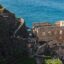 Castle ruins perched on a cliff next to the see with lush greenery surrounding it.