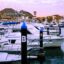 An image of boats lined up at the dock in San Jose del Cabo Marina, with purple and pink skies behind.