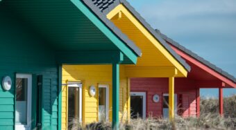 one small green wooden house in the foreground, with one small yellow wooden house behind it and another small red house behind that