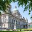 grand white government building with green copper roof and statue in the garden in front of building