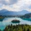 bright blue waters surrounding a small island of trees with mountains under a cloudy sky