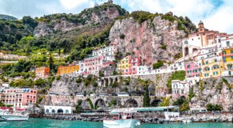 sprawling cliff with colorful buildings built upward alongside bright waters and a boat in the water