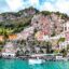 sprawling cliff with colorful buildings built upward alongside bright waters and a boat in the water